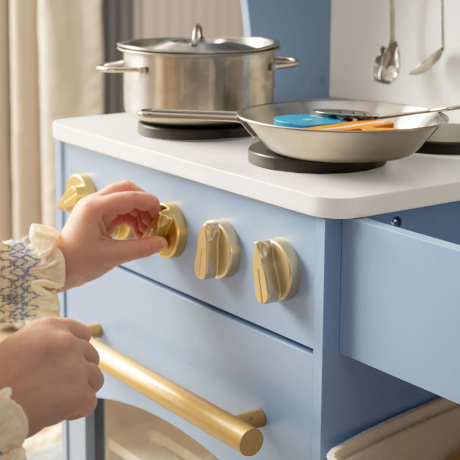 Close-up of a child's hand turning knobs on a toy kitchen stove.