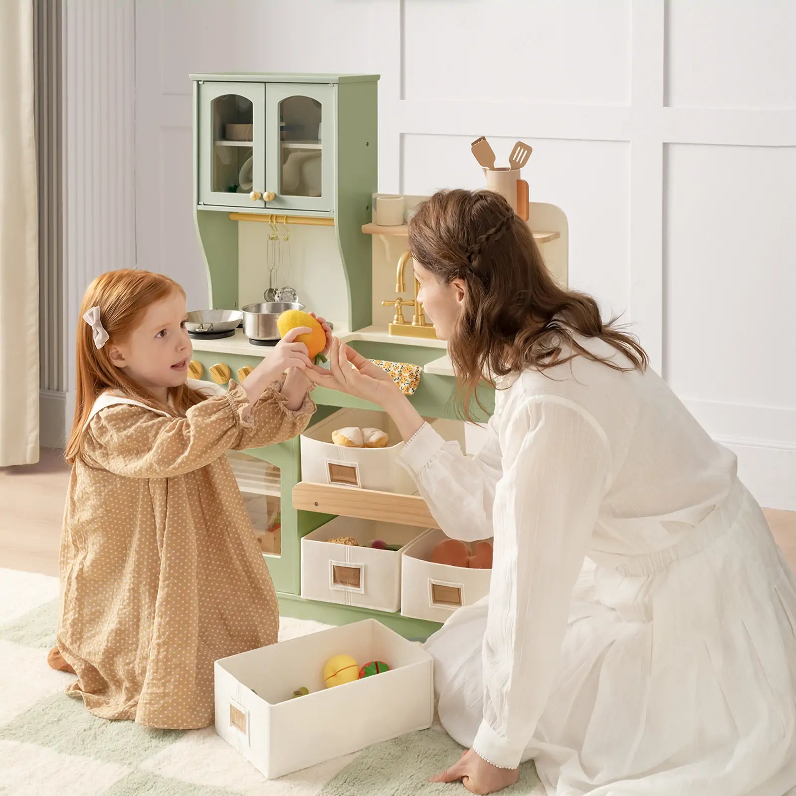 Child and adult interacting with a green play kitchen, holding toy food items